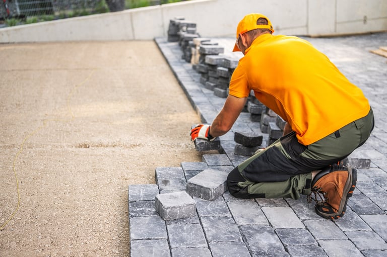 A construction worker carefully positions cobblestones to create a new patio in a residential yard